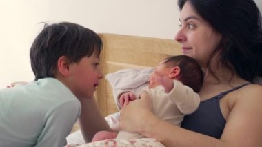 Anne bebeğini kucağında tutarken, büyük kardeş bakmak için eğilip birbirine bağlı aile bağını ön plana çıkarıyor. Sahne sıcaklığı, ilgiyi ve anne ile çocuk arasındaki sevgi bağını yansıtıyor.