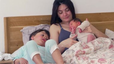 Anne, büyük kardeş yanında yatarken bebeğini kucağına alır. Sahne huzurlu bir aile anını yakalıyor. Sevgiyi ve anne ile çocuk arasındaki bağı yansıtıyor.
