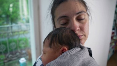 Anne, yeni doğmuş bebeğini omzuna almış, gözleri dingin bir şekilde bağlanmış. Anne ve çocuk arasındaki derin bağ ve sıcaklık.