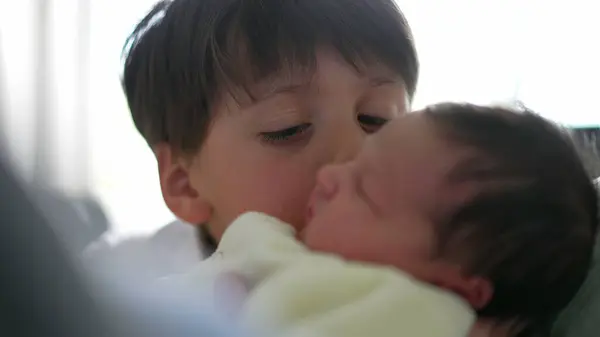 Stock image Young boy gently kissing his newborn sibling, expressing pure affection and love. The closeness and focus on their faces highlight the strong bond and tender relationship between them