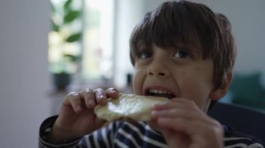 Huzurlu bir yuva - Sevimli bir çocuk peynirli ekmeğin tadını çıkarıyor, atıştırmalık bir şeyler yemenin hazzı ve tatmini üzerine odaklanıyor, neşeli bir çocukluk anını yakalıyor.