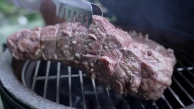 Barbekü ızgarasında terbiye edilmiş et pişirmek, ızgara yapma sanatını sergilemek ve enfes sonuçlar elde etmek, dumanın yükselmesi ve lezzetlerin artırılması, açık hava bahçe ortamında, yakın çekim manzarası...
