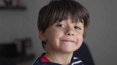 Yaramaz bir gülümsemesi ve çizgili tişörtü olan, çocukluk eğlencesi, masumiyet ve neşe teması için mükemmel bir ifade sergileyen, rahat bir ev ortamında yakalanan genç bir çocuk.