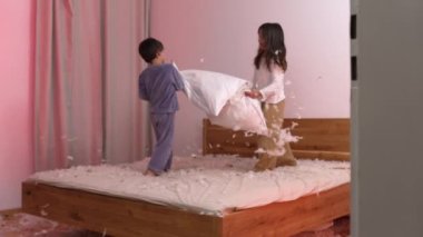 Yatakta dinamik bir yastık kavgası yapan iki çocuk, her yerde uçuşan tüyler, hem gülen hem de eğlenen, rahat bir ev ortamında rahat pijama giyen iki çocuk.