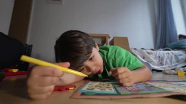 Yerlere sarı işaretli çizim yapan, ev dekorasyonu yapan, boyama kitabına odaklanan, yeşil tişört giyen, yaratıcı ve eğitici oyun oynayan, kapalı alan, doğal ışık, çocukluk gelişimi...