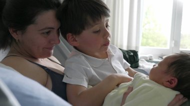 Anne ve büyük kardeş hastane yatağında yeni doğan bebeğe nazikçe hayran. Aile anlarında kardeşlerin sıcaklığı ve bağlantıları vurgulanıyor. Anne şefkati, aile neşesi ve birlikteliği vurgulanıyor.