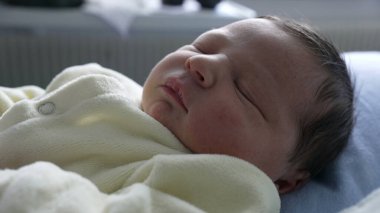 Yeni doğmuş bebek yumuşak bir kıyafetle dinlenirken parmağına tutunuyor. Yakın plan, küçük, narin eli ve hassas anı yakalar. Yetiştirici bir ortamda doğan bir bebeğin hassasiyetini ve masumiyetini vurgular.