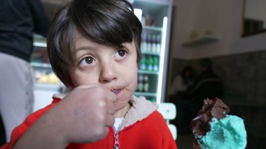 Düşünceli bir ifadeyle dondurma yiyen çocuk, çocukluk hoşgörüsünü ve merakını temsil ediyor, yüzünü ve elini kapalı bir dondurmacıda gösteriyor.