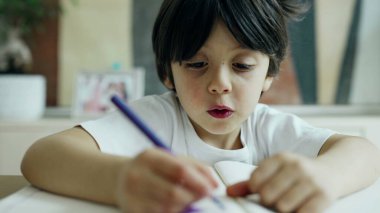 Mavi kalemle çizen çocuk, yaratıcılık sürecine odaklanmış, ev ortamında yakalanmış, çocukluk sanatsal aktivitelerinin neşe ve konsantrasyonunu vurguluyor