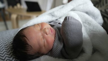 Yeni doğan bebek, huzurlu bir şekilde dinlenirken rahat bir battaniyeye sarılıp esniyor. Huzurlu bir ortamda yeni doğan bir bebeğin yumuşak ve hassas doğasını vurguluyor.