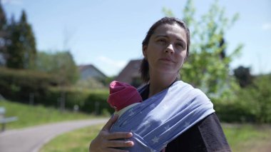 Yeşilliklerle çevrili, mavi bir bebek şalıyla gezen anne, ebeveynler ve çocuklar arasındaki sevgi ve sevgiyi gösteriyor, dışarıda huzurlu bir günün tadını çıkarıyor.