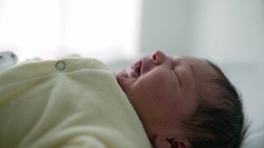 Yeni doğmuş bebek yumuşak bir yüzeyde, rahat bir krem kıyafet içinde yatıyor. Bebeğin yüzündeki sakin ve sakin ifade bir huzur ve masumiyet duygusu taşır, erken yaşların ve aile temalarının özünü yakalar.