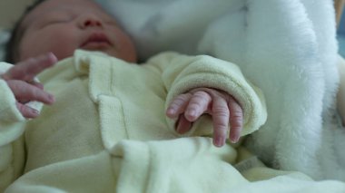 Yeni doğmuş bir bebeğin küçük elinin, yumuşak, beyaz bir battaniyeye sarılı olarak, bebeğin narin ve nazik doğasını, ve yaşamın ilk günlerinde sunulan sıcaklığı ve bakımı yakalıyor.