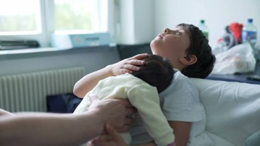 Çocuk, hastane odasında ebeveyn desteğiyle yeni doğan bebeği beşikte, kardeş bağını, aile sevgisini ve yetiştirme ortamını sembolize ediyor.