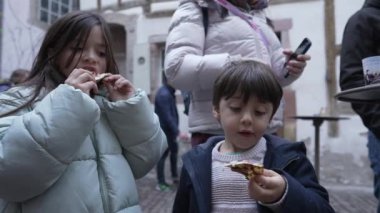 Çocuklar açık hava pazarında pizzanın tadını çıkarıyorlar, keyifli bir atmosferde taze ve lezzetli yiyeceklerin tadını çıkarıyorlar, birlikte yemek yemenin ve unutulmaz bir deneyimi paylaşmanın keyfini çıkarıyorlar.