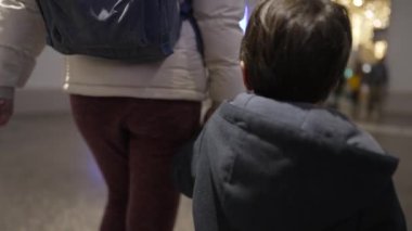 Günlük Annelik Sorumluluğu - Çocuklar Bir Tren İstasyonunda, Kışlık Paltolarda ve Sırt Çantalarında, Parlak Işıklı Terminalde, Arka planda, Yolcular
