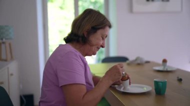 Evde Oeuf la coque 'un keyfini çıkaran yaşlı bir kadın günlük rutininde bir huzur ve sıcaklık anı yaratıyor. Ailesini ve basit zevkleri vurguluyor.