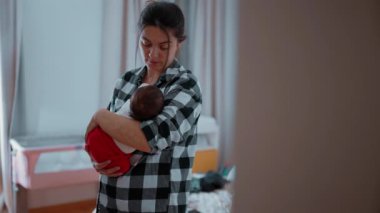 Anne, huzurlu bir yatak odasında bebeğini nazikçe kucaklıyor. Bebek yumuşak bir battaniyeye sarılmış, kendini güvende ve sevilmiş hissediyor.