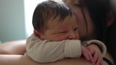 Anne, yeni doğmuş bebeği yanağından öpüyor. Hassas an, yumuşak ışıklandırmalı sıcak bir ev ortamında geçen derin bir sevgi ve bağı yakalar.