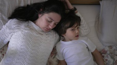 Anne ve küçük çocuk yatakta yatıyor, anne çocuğun alnından nazikçe öpüyor, huzurlu ve sevgi dolu bir aile anını yakalıyor, ebeveyn-çocuk ilişkisine odaklanmak için ideal bir yaşam tarzı.