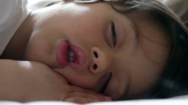 Çocuk yatakta huzur içinde uyuyor, çocukluk uykusunun sükunetini ve sükunetini gösteriyor, yumuşak ve sakin bir ifadeyle, huzurlu ve güvenli bir çevreyi vurguluyor.