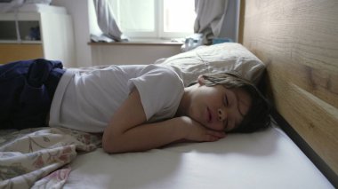 Çocuk tek başına uyuyor, huzur içinde kıvrılıyor, rahat ve güvenli bir uyku alanının huzurlu ve sakin ortamını vurguluyor, yumuşak sabah ışığıyla.