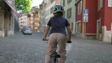 Kasklı bisikletli bir çocuk renkli binaları olan eski şehir caddesinde geziyor, tarihi şehir ortamlarında açık hava maceraları sergiliyor ve aktif bir çocukluk geçiriyor, yaşam tarzı görüntüsü için ideal.