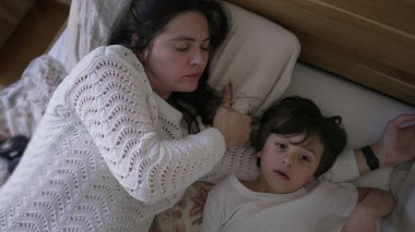 Anne ve küçük çocuk yatakta yatıyor, anne çocuğun alnından nazikçe öpüyor, huzurlu ve sevgi dolu bir aile anını yakalıyor, ebeveyn-çocuk ilişkisine odaklanmak için ideal bir yaşam tarzı.