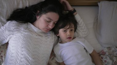 Anne ve küçük çocuk yatakta yatıyor, anne çocuğun alnından nazikçe öpüyor, huzurlu ve sevgi dolu bir aile anını yakalıyor, ebeveyn-çocuk ilişkisine odaklanmak için ideal bir yaşam tarzı.