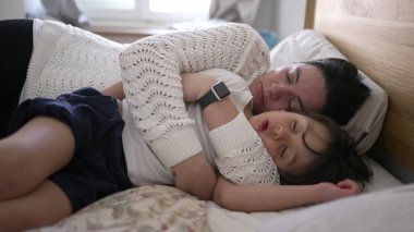 Anne ve küçük çocuk yatakta uzanıyor, kucaklaşıp huzur içinde uyuyor, aile bağlarının rahatlığını ve yakınlığını vurguluyor, ebeveyn-çocuk ilişkilerine odaklanmış yaşam tarzı için ideal.