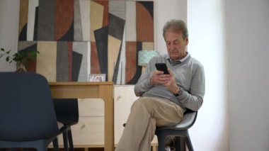 Yaşlı adam akıllı telefonuyla derinden meşgul. Sanatsal dekor ve doğal ışık, çağdaş teknolojiyle olan bağlantısını vurgulayarak, sıcak ve modern bir ortam yaratıyor.