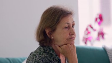 Düşünceli bir ifadeyle, çenesini eline dayamış yaşlı bir kadının yan görüntüsü. Doğal ışık ve yumuşak arka plan onun düşünceli ve sakin tavrını geliştirir.