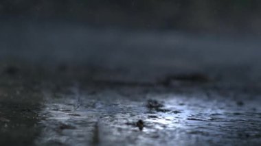 Yağmur damlalarının yere yavaş çekimde 1000 fps hızla düşmesi, sıçrama efektlerini ve su desenlerini göstermesi, yağmurun güzelliğini ve hareketini vurguluyor.