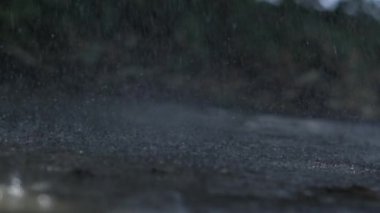 Yağmur damlaları yere yavaş çekimde 1000 fps hızla çarpıyor, su sıçramalarının karmaşık desenlerini ve dokusunu gösteriyor, yağmurun doğal güzelliğini ve dinamiklerini vurguluyor.