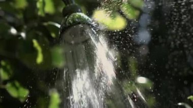 Su spreyini yavaş çekimde 1000 fp 'de yakın çekim, güneş ışığı bir dizi damlacık oluşturarak, açık hava ortamında dokuyu ve sıvı dinamiğini vurguluyor.