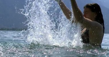 800 fps 'de kollarını kaldıran ve su sıçratan bir kadın dingin bir göl ortamında hareketli ve eğlenceli bir görüntü sergiliyor.