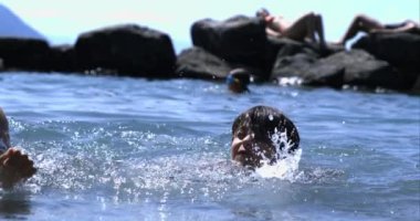 Çocuk gölde yüzüyor ve su sıçrıyor, neşeli bir ifade, su damlacıkları yavaş çekimde 800 fps, yaz eğlencesi, arka planda kayalar