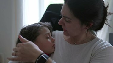 Kafası yaralanan çocuğunu teselli eden, onu nazikçe kucaklayan, şefkatli bir ifade gösteren, içten ve samimi bir anne sevgisi ve destek anı yaşayan endişeli bir anne.