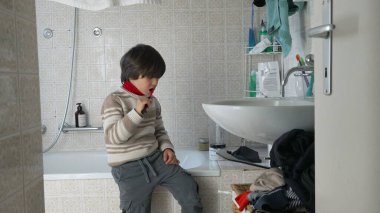 Genç bir çocuk banyoda dişlerini fırçalıyor, elinde diş fırçasıyla lavabonun yanında duruyor, rutin bir sabah aktivitesini ve sağlıklı hijyen alışkanlığını canlandırıyor.