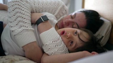 Anne ve küçük çocuk yatakta uzanıyor, anne huzur içinde uyuyor ve çocuk yavaşça uykuya dalıyor, huzurlu ve samimi bir aile anını yakalıyor, yaşam tarzı için mükemmel.
