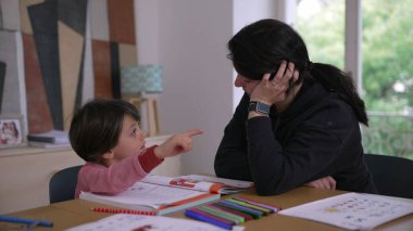 Annesi rehberlik, renkli kalemler ve eğitici materyaller sunarak destek veren ebeveynlik ve erken eğitimi gösteren küçük çocuk ödevlerini dikkatle yapıyor.