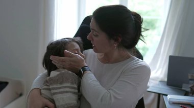 Kafası yaralanan çocuğunu teselli eden, onu nazikçe kucaklayan, şefkatli bir ifade gösteren, içten ve samimi bir anne sevgisi ve destek anı yaşayan endişeli bir anne.