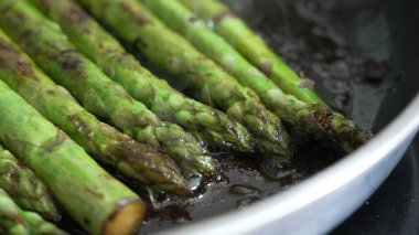 Izgara kuşkonmaz mızrakları tavada cızırdıyor, canlı yeşil renkler ve karamelize kenarları sergiliyor, taze sebze görüntüsü arayan mutfak ve yemek fotoğrafçıları için mükemmel.