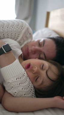 Anne ve çocuğu yatakta birlikte kestiriyorlar, bağlarının sıcaklığını ve yakınlığını gösteriyorlar. Yumuşak ışıklandırma ve rahat battaniyelerle sakin bir atmosfer, huzuru artırır.