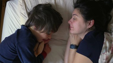 Anne ve oğul, sıcak ve sevgi dolu bir ortamda, samimi ve neşeli bir anı paylaşarak, yatakta uzanıyorlar.