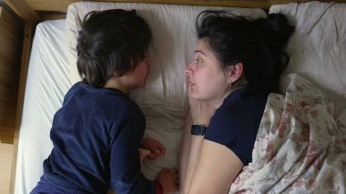 Anne ve oğul, sıcak ve sevgi dolu bir ortamda, samimi ve neşeli bir anı paylaşarak, yatakta uzanıyorlar.