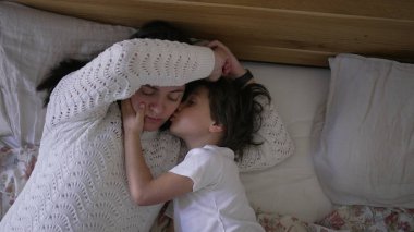 Anne ve küçük çocuk yatakta uzanıp, sevgi dolu bir anı paylaşırken, çocuk annesine sarılıp onu öperken, ebeveyn ve çocuk arasındaki sevgi ve bağın altını çizerken, yaşam tarzı fotoğrafçılığı için mükemmeldir.