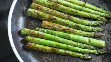 Buhar yükselen bir tavada taze kuşkonmaz pişirme, taze malzemelerin ve sağlıklı pişirme tekniklerinin kullanımını vurgulama, canlı rengi ve sebzenin besleyici değerini vurgulama,