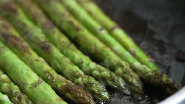 Izgara kuşkonmaz mızrakları tavada cızırdıyor, canlı yeşil renkler ve karamelize kenarları sergiliyor, taze sebze görüntüsü arayan mutfak ve yemek fotoğrafçıları için mükemmel.