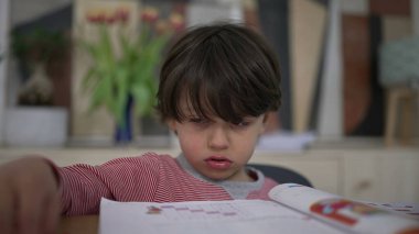 Genç çocuk, okul aktivitelerinden gözle görülür şekilde hayal kırıklığına uğramış ama yine de kararlı. Çalışmasını tamamlamak için bir kalem alıyor, direnç gösteriyor ve zorluklara rağmen öğrenmeye odaklanıyor.